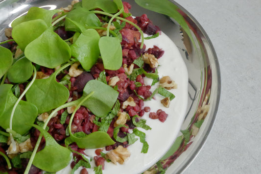 Dish with whipped feta, beetroots, and green leaves on a metal plate.