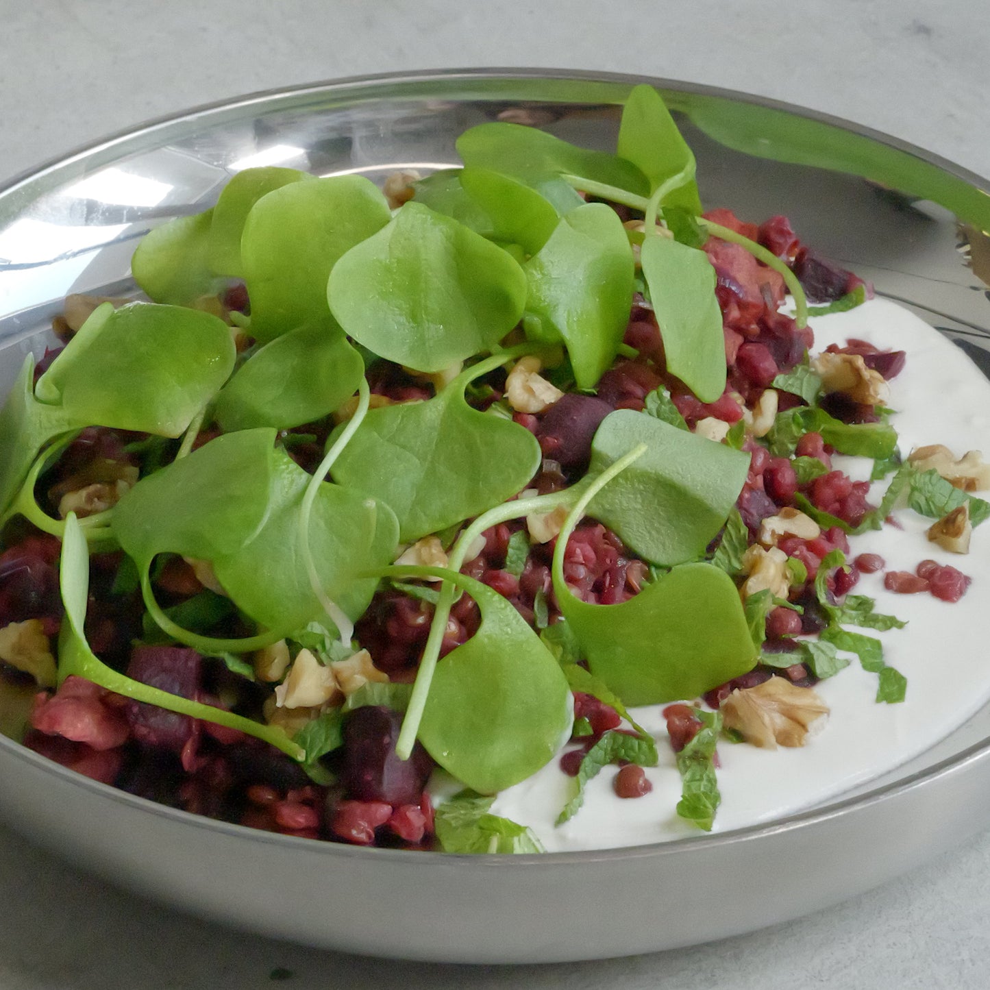Salad with greens and beetroots in a metallic bowl on a light gray surface