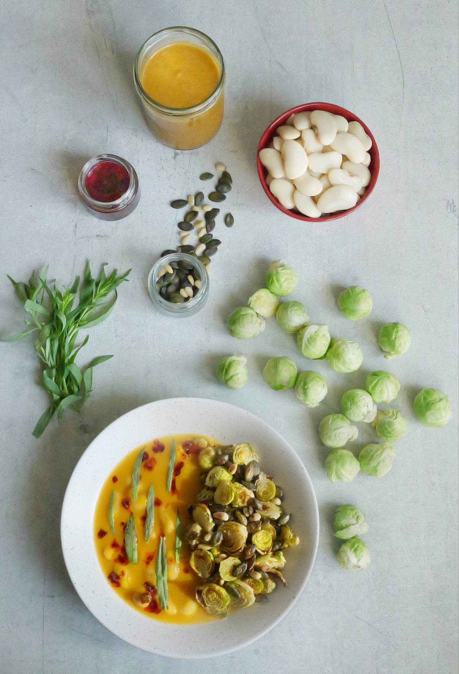 Plate of food with ingredients including brussels sprouts, a jar of sauce, and small containers on a light surface.